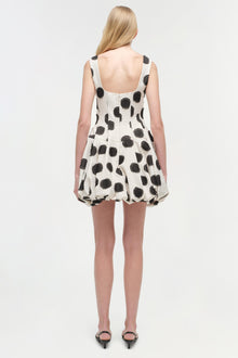Sleeveless mini dress with black polka dots on cream fabric, open back design, shown from behind on model.