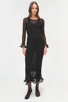 Black metallic plisse long-sleeve top with sheer mesh panels and ruffled cuffs worn with matching midi skirt.