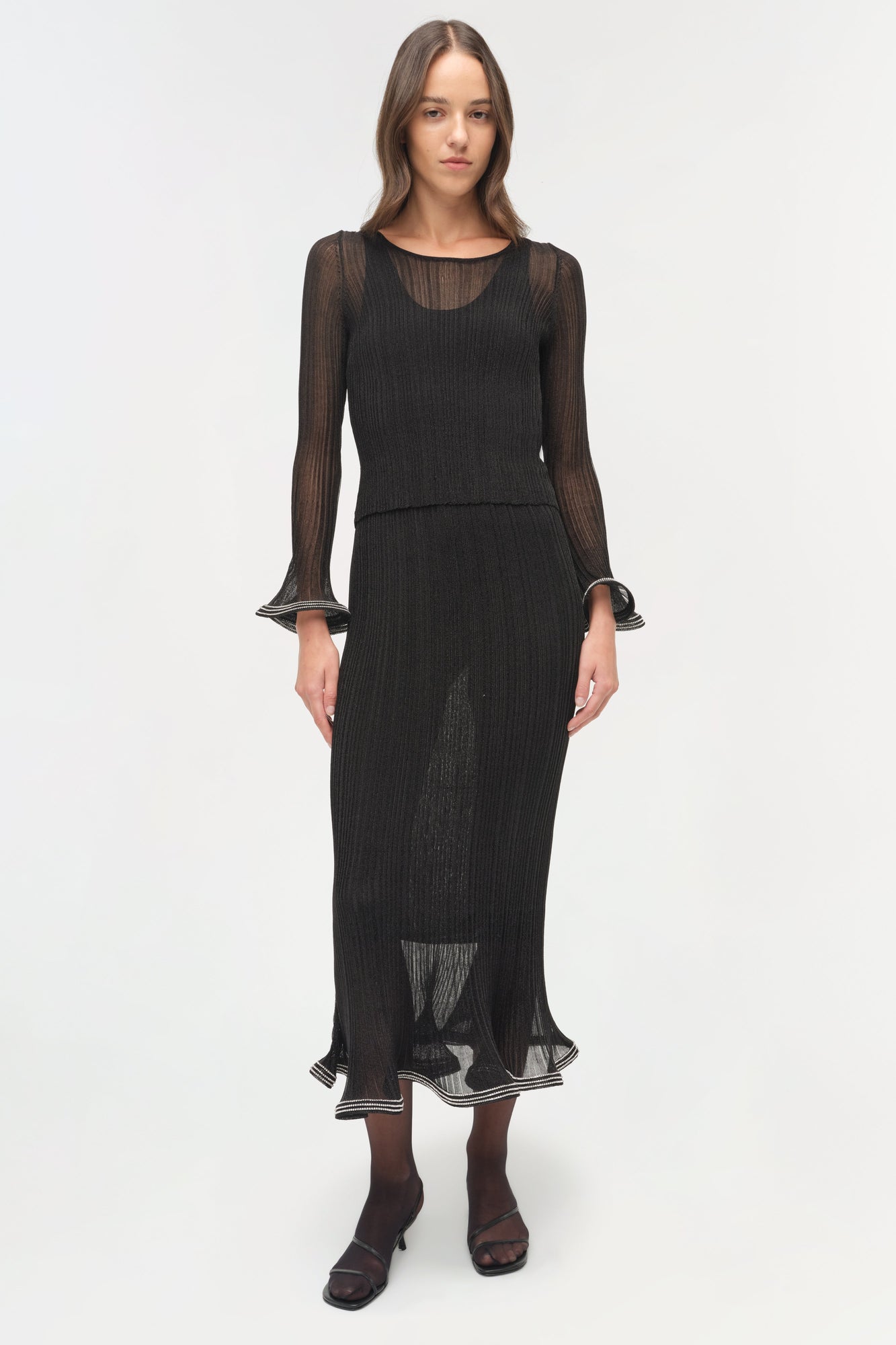 Black metallic plisse long-sleeve top with sheer mesh panels and ruffled cuffs worn with matching midi skirt.