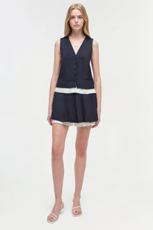 Woman wearing a navy pleated skort with white trim and matching buttoned vest over a white striped band.