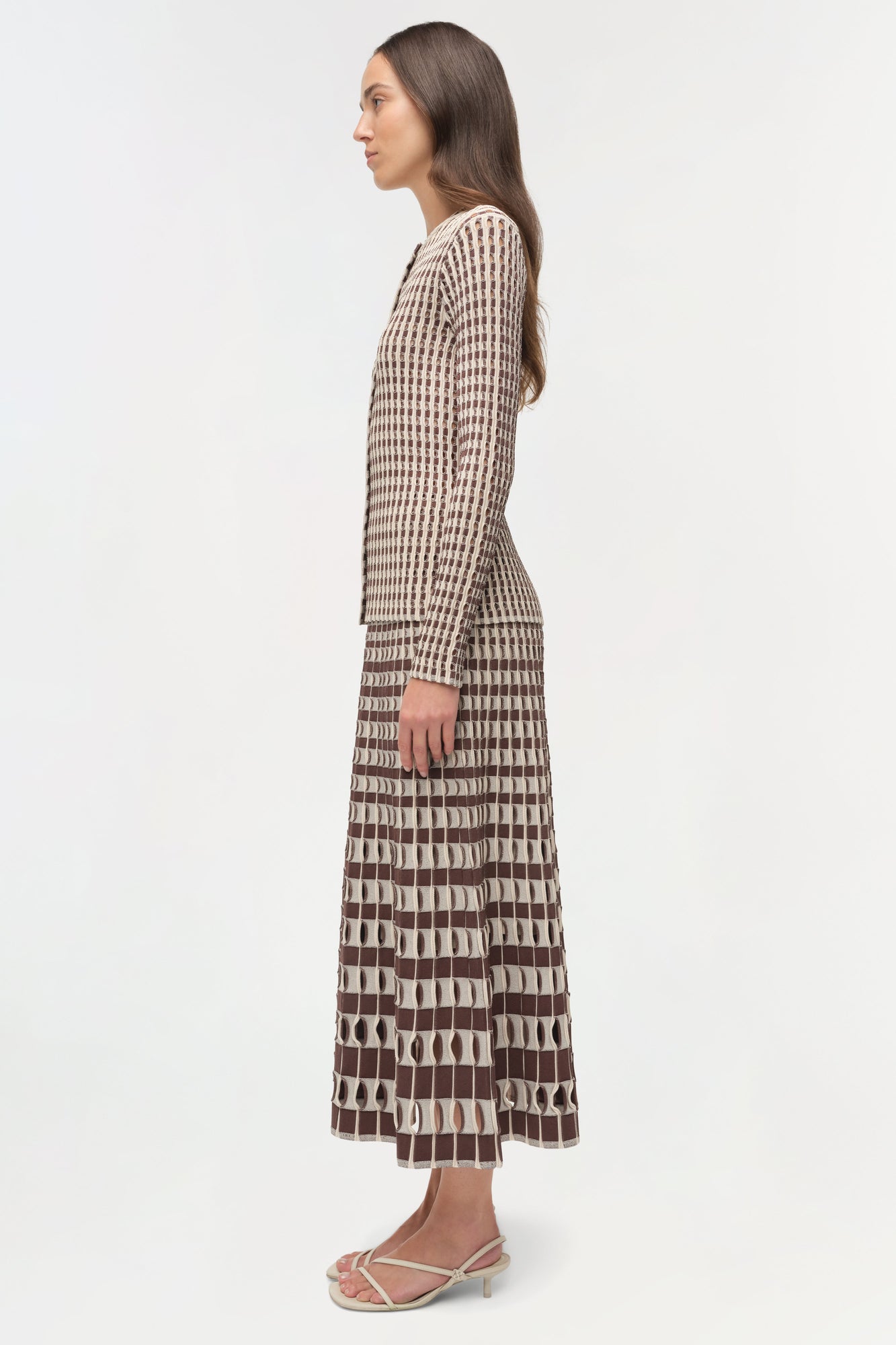 Woman wearing a brown and cream ribbed knit cardigan with geometric patterned skirt, shown from the side.