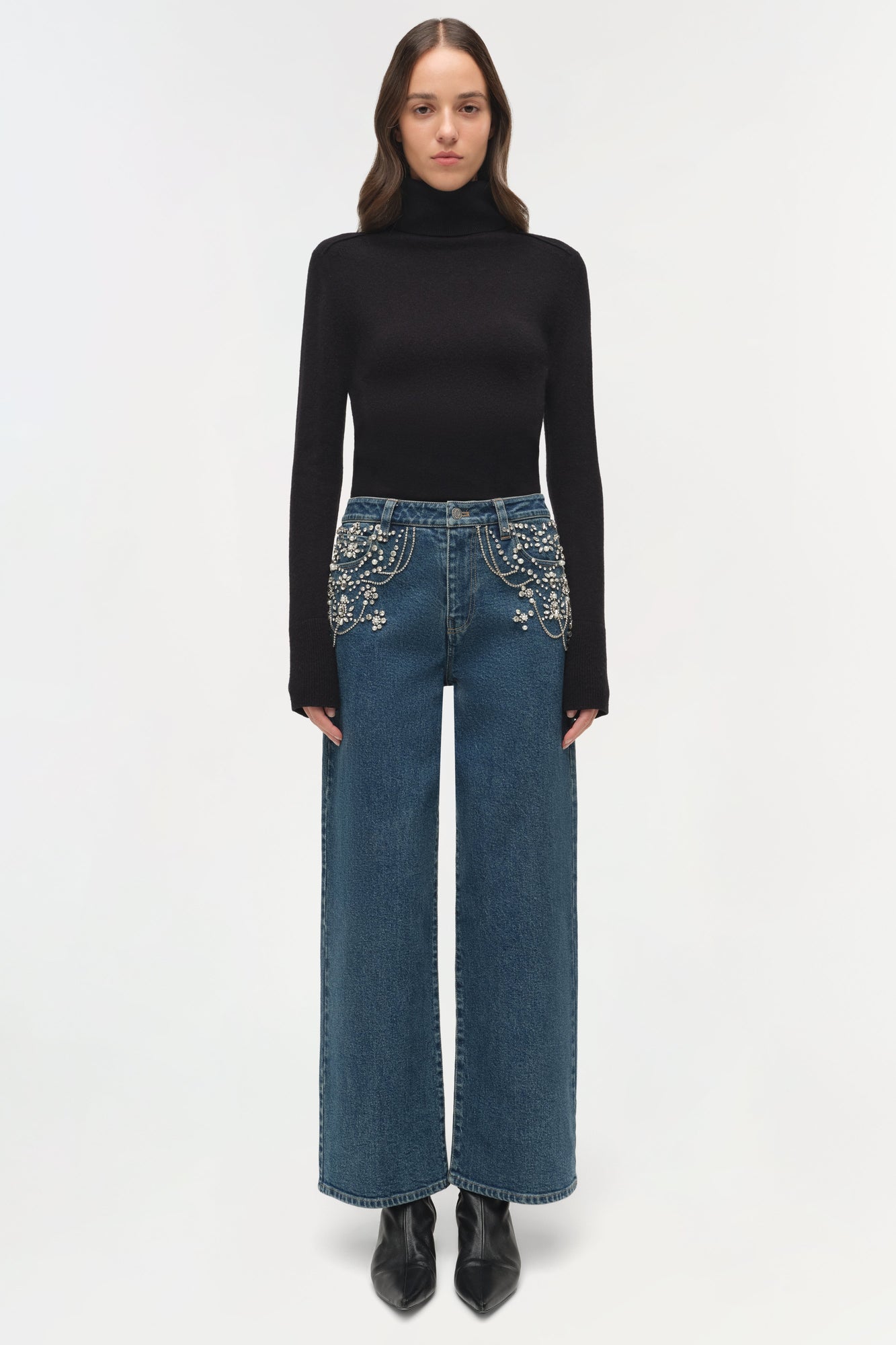 Blue denim crop jeans with pearl embellishments on pockets, paired with black turtleneck and boots.