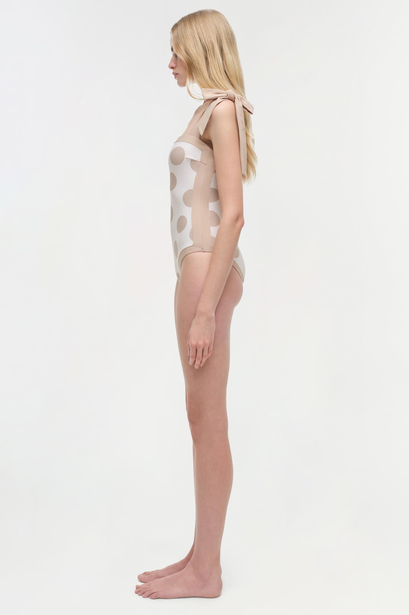 Woman wearing cream one-piece swimsuit with tan polka dot pattern, shown from the side.