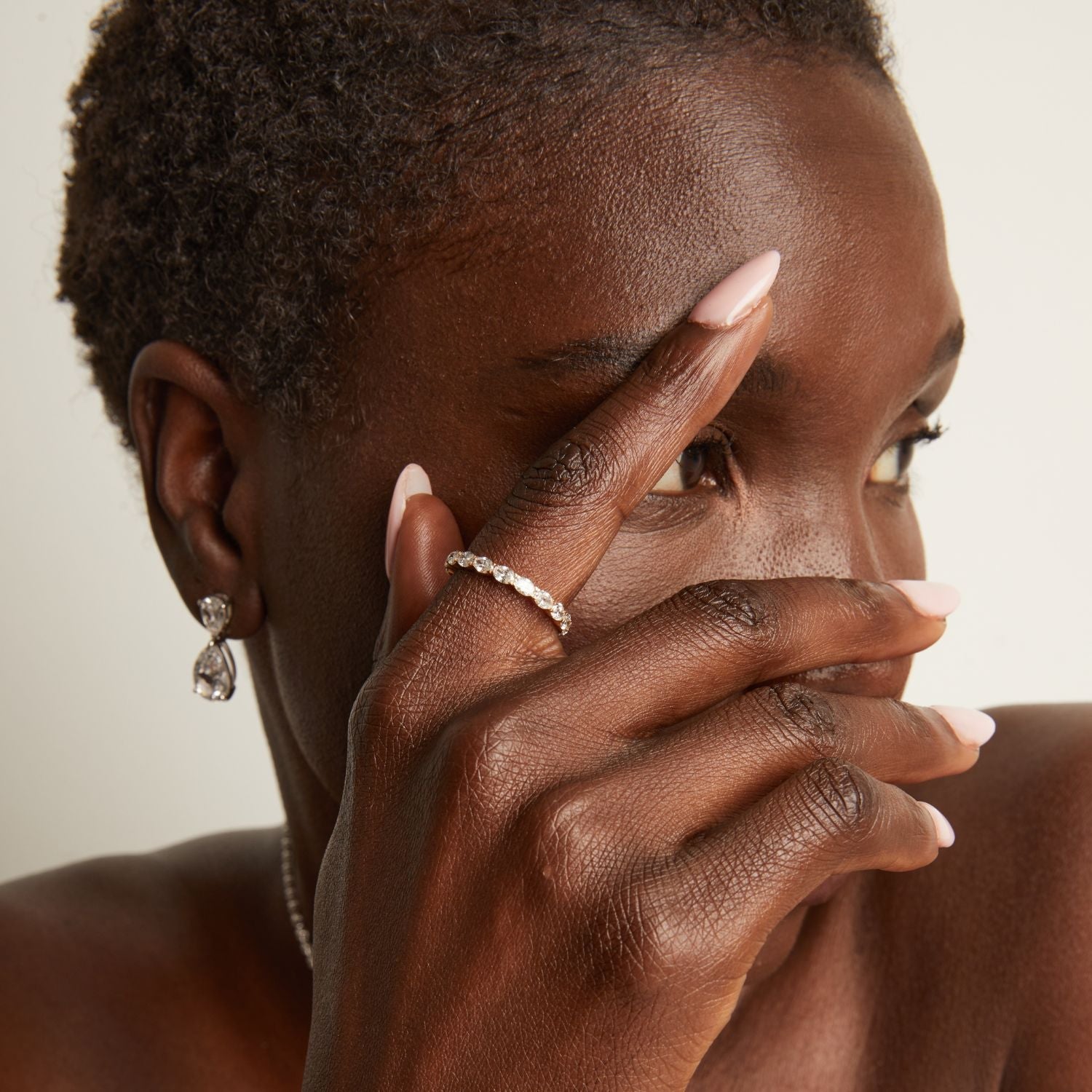 Model. Woman wearing earrings and a ring with a neutral background
