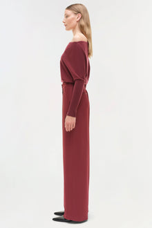 Woman wearing burgundy satin wide-leg pants with off-shoulder top and black shoes, shown in profile view.