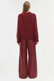 Woman wearing burgundy crewneck cashmere sweater with ribbed cuffs and matching wide-leg pants, shown from back.