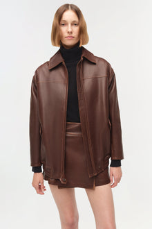 Brown leather oversized jacket with wide collar, full-length sleeves, and front zip closure worn over black turtleneck.