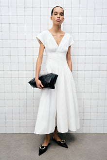 White cotton midi dress with V-neckline, short sleeves, and gathered waist on model wearing black pointed flats.