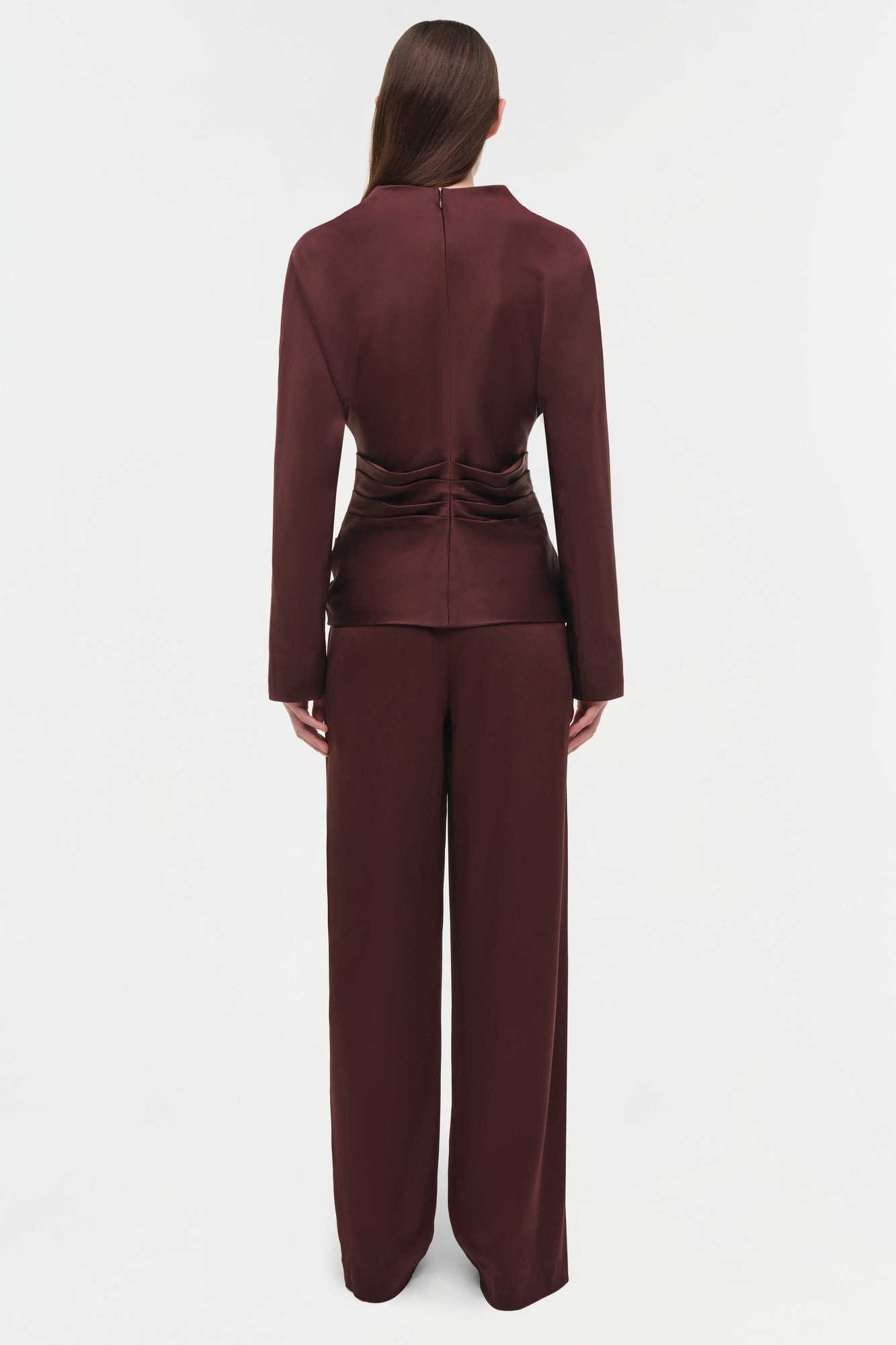 Woman wearing burgundy draped satin top with ruched waist detail and matching wide-leg pants, shown from back.