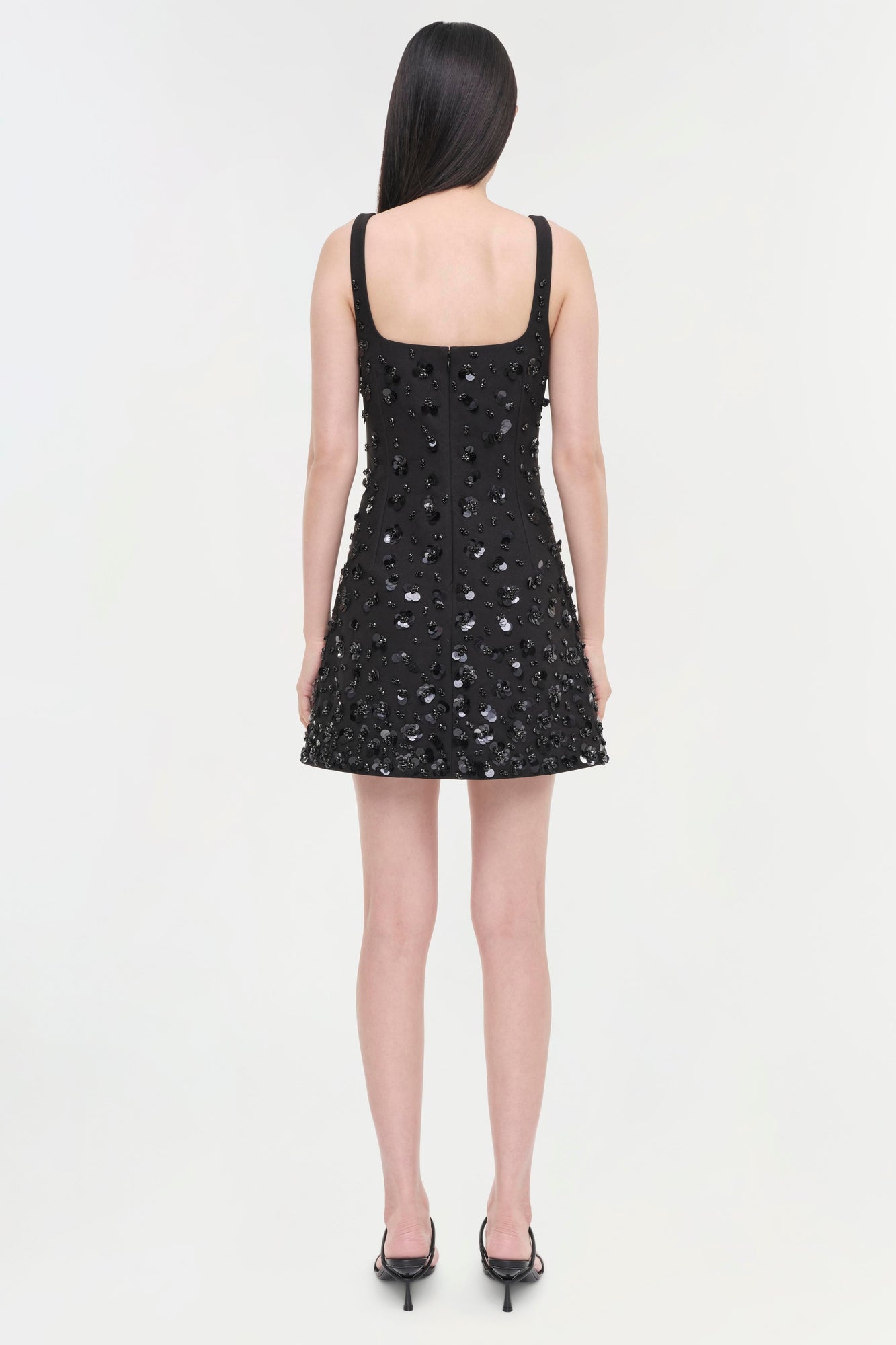 Black sequined sleeveless mini dress with square neckline, shown from back view on model wearing black heels.