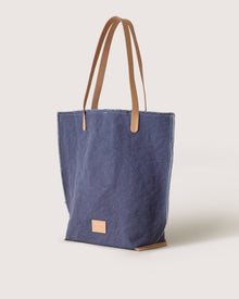 The graf lantz Hana Canvas Tote is made from sturdy cotton canvas with tan leather handles and a small front leather patch. It stands upright against a white background, highlighting its elegant blend of functionality and style.