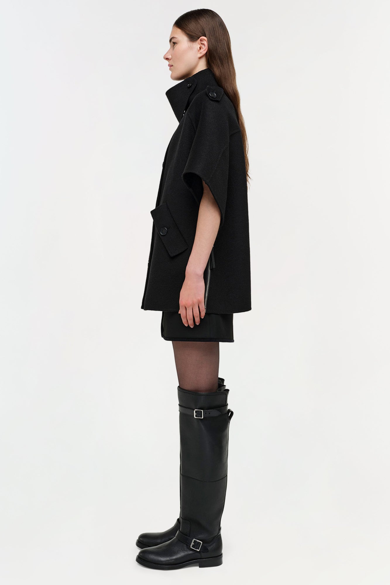 Black wool cape jacket with button closures worn with matching dress and tall black boots.