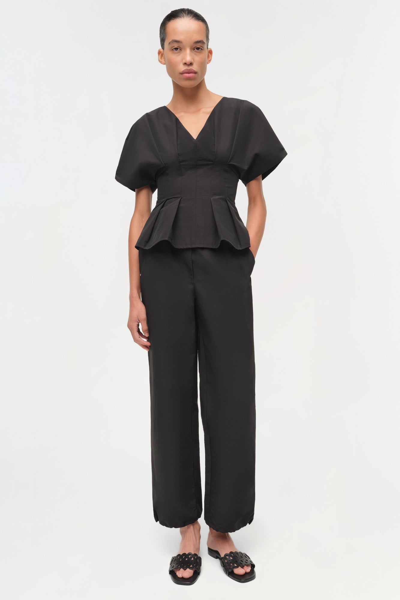 Black cotton faille top with V-neckline, short puffed sleeves, and structured peplum waist detail.