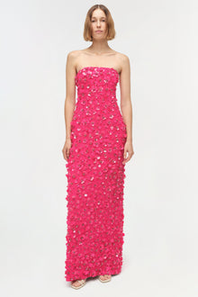 Woman wearing a hot pink strapless floor-length gown covered in sequin embellishments.