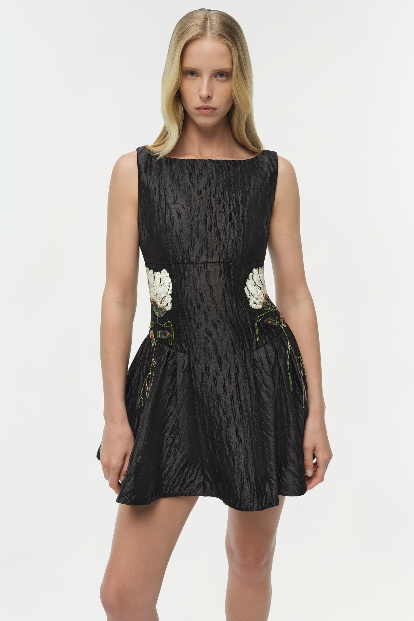 Black jacquard mini dress with white floral embroidery appliquÃ©s at the waist and green leaf embroidery details on the skirt.