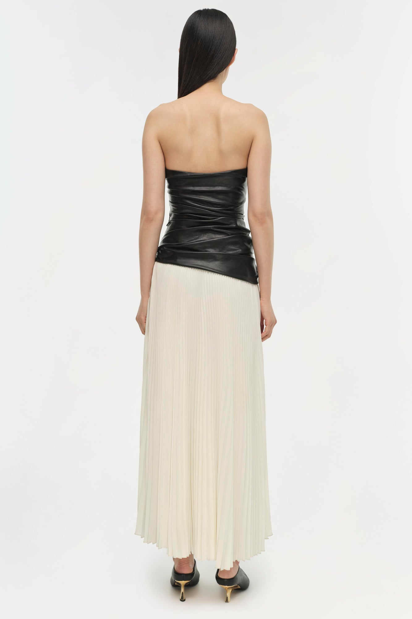 Strapless dress with ruched black leather bodice and ivory pleated skirt, back view.