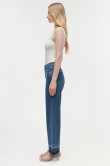 Woman wearing a white sleeveless tank top and blue wide-leg cropped jeans with a raw hem.