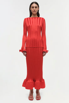 Red ribbed knit top with long sleeves, ruched cuffs, and a cropped silhouette worn with matching maxi skirt.