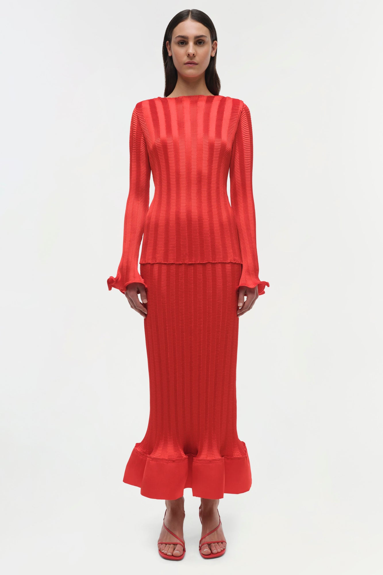Red ribbed knit top with long sleeves, ruched cuffs, and a cropped silhouette worn with matching maxi skirt.