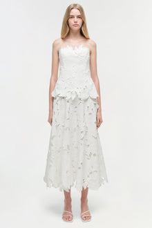 White strapless midi dress with leaf-shaped embroidered cutout details throughout, worn with white sandals.