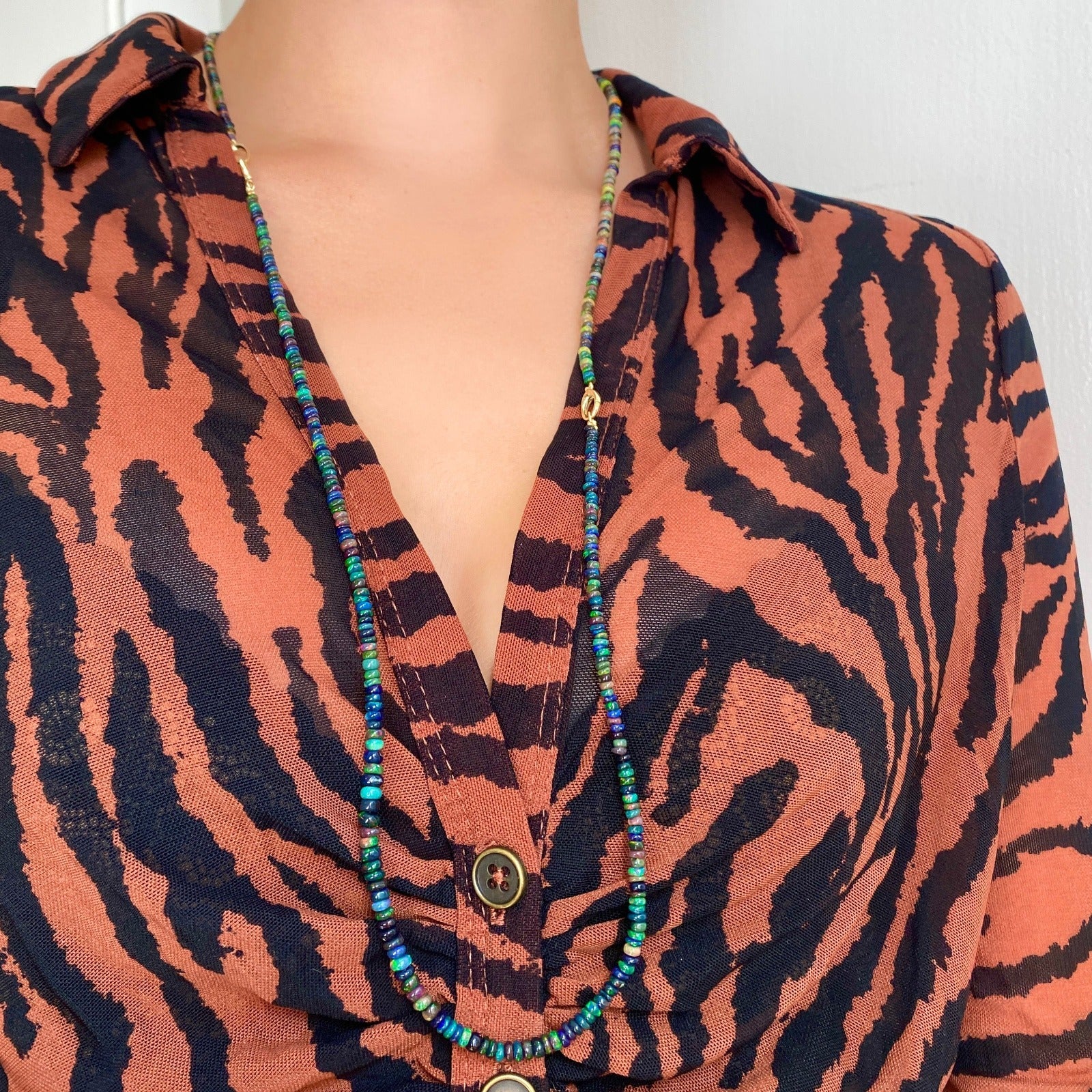 Shimmering beaded necklace made of smooth opal rondels in shades of black, navy, and green on a slim gold lobster clasp.