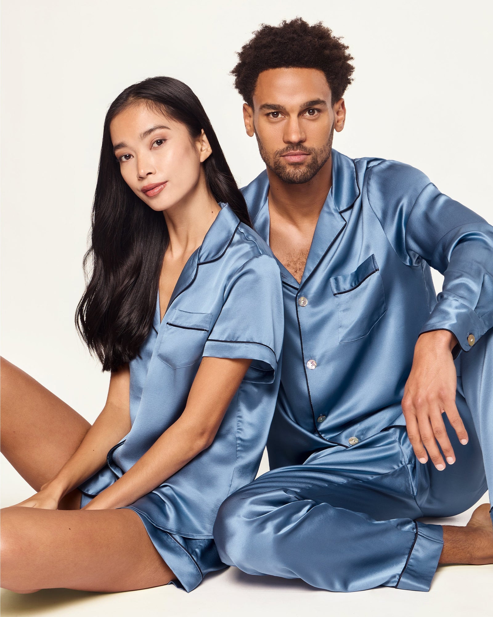 The Men's Silk Pajama Set in Mystique Blue features a button-up long-sleeve top with a chest pocket and matching elastic-waist pants, both trimmed with dark piping.