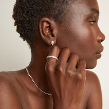 Model. Woman wearing an eternity ring and drop earrings on a neutral background