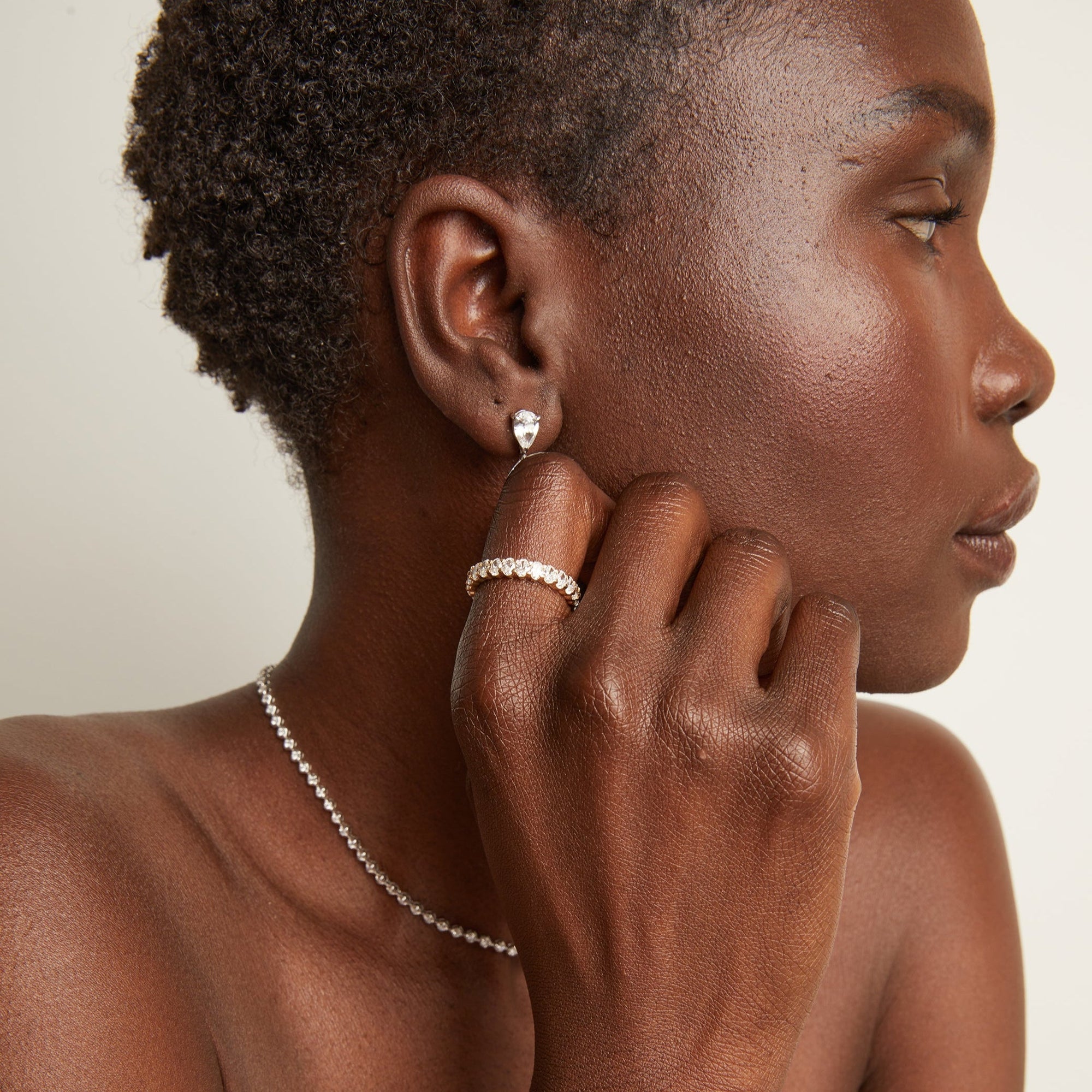 Model. Woman wearing an eternity ring and drop earrings on a neutral background