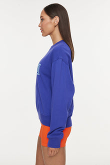 Model wears a royal blue crewneck sweatshirt with the lettering 