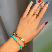 Shimmering beaded bracelet made of smooth opals in shades of bright blue on a gold linking lobster clasp. Styled on a wrist with a diamond cut link chain bracelet.