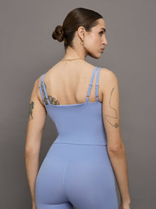 Model wears a periwinkle colored cropped v neck tank top with double straps on the back. 
