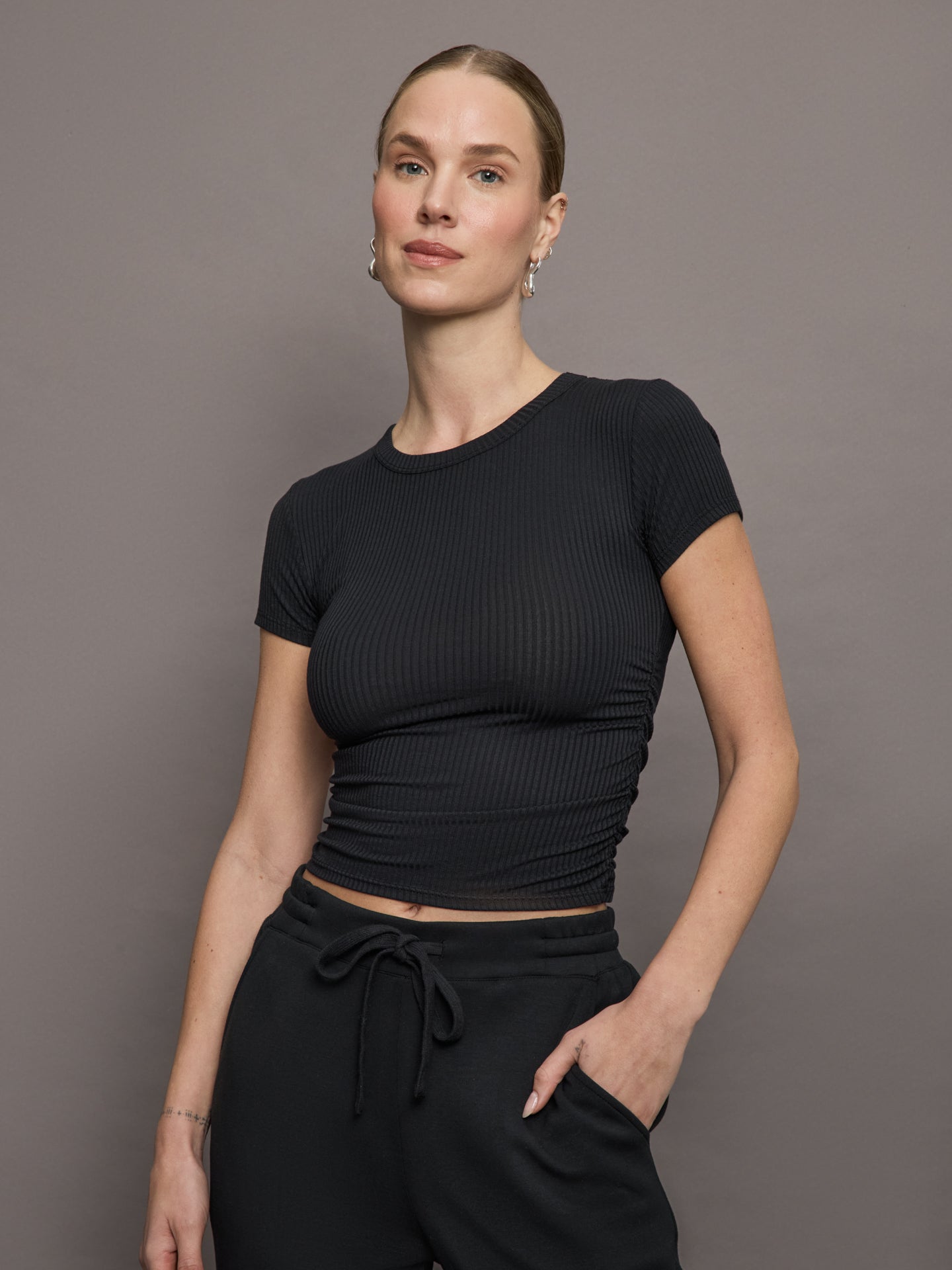 Model wears a short sleeved, ribbed jersey fitted black top with ruching down both sides. 