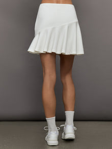 Model wears a white tennis skirt with an asymmetrical ruffle and built in shorts.