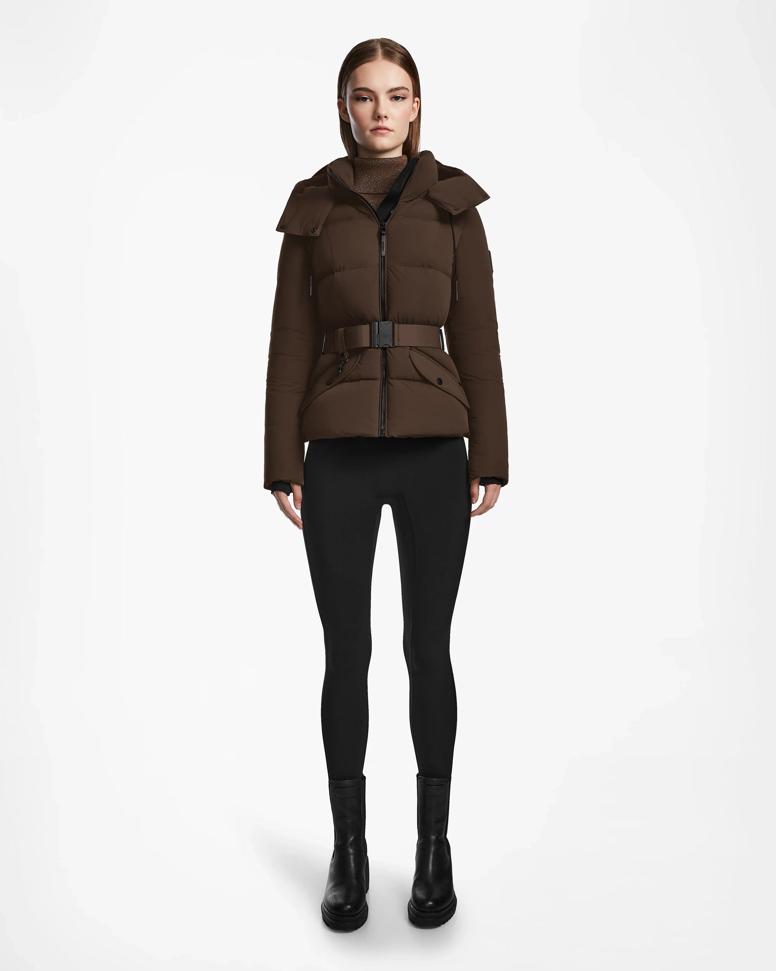 A woman faces forward wearing the Rudsak ADELINE - 8124544 Mocha quilted short down puffer jacket with a belt, paired with black leggings and black ankle boots against a plain white background.