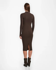 A woman with straight brown hair wears the Rudsak AGNES - 8524551 Espresso fitted, long-sleeve, dark brown bodycon dress and black ankle boots, standing and facing away from the camera against a white background.