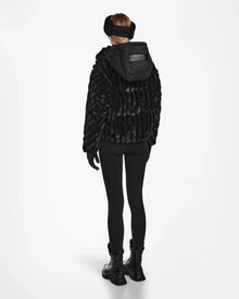 A person faces away, wearing the Rudsak ANASTASIA - 8124804 Black faux fur hooded winter coat with black earmuffs, leggings, gloves, and combat boots against a plain white background.