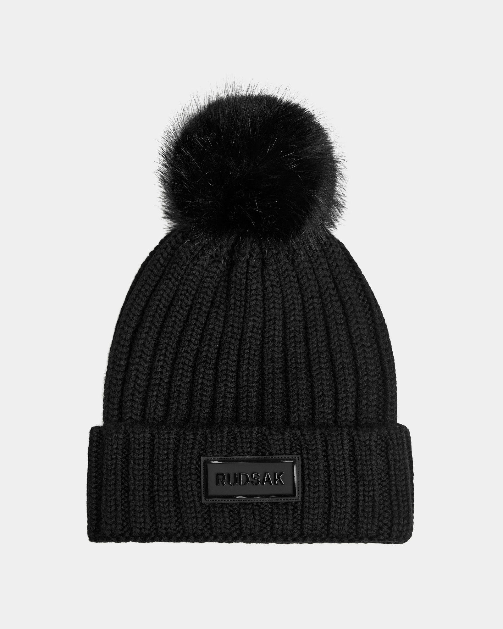 The Rudsak ANISA - L423500 Black/Black beanie features a ribbed knit design, large faux fur pom pom, folded cuff, and a rectangular Rudsak label—perfect for any winter wardrobe.