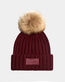 The ANISA - L423500 Wine by Rudsak is a maroon ribbed knit women’s beanie with a wide folded brim, brown faux fur pom pom, and a front rectangular Rudsak patch—perfect for adding style to your winter look.