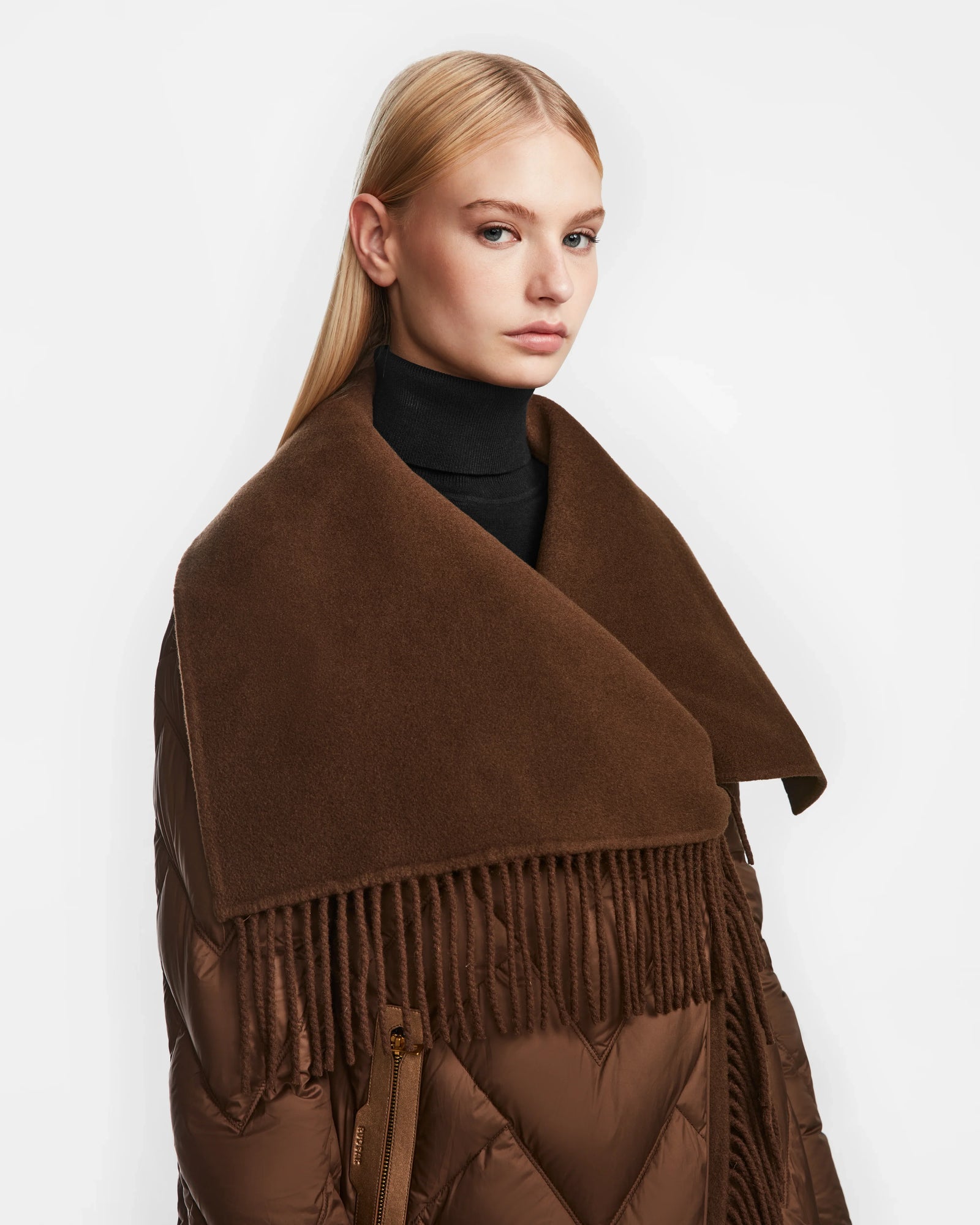 A woman with straight blonde hair wears a black turtleneck and the Rudsak ANNE MARIE - 8124713 Mocha relaxed fit jacket with an oversized shawl collar and long fringe, embracing the western trend against a plain white background.