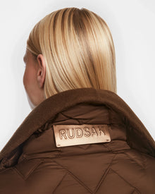 A person with straight blonde hair is shown from the back, wearing the Rudsak ANNE MARIE - 8124713 jacket in mocha quilted fabric with a large collar, featuring a beige Rudsak label prominently displayed on the collar.