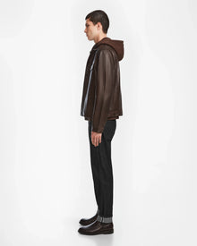 A young man stands in profile against a white background, wearing the Rudsak AREN - 6124580 Espresso jacket over a brown hoodie, paired with dark jeans and brown boots.
