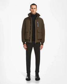 A man faces forward in an urban style, wearing the Rudsak ASH - 6124599 Army brown winter jacket with large pockets, a black turtleneck, black pants, and black boots against a plain white background.