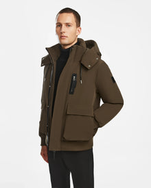 A man wearing the Rudsak ASH - 6124599 Army mens down bomber jacket with large front and zippered chest pockets over a black turtleneck, standing against a white background. This winter jacket is insulated with RDS-certified down for warmth.