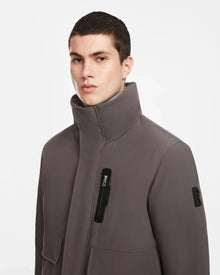 A young man with short dark hair wears the Rudsak ASH - 6124599 Grey winter jacket, featuring a high collar, zippered chest pocket, and a sleeve patch, standing against a plain white background.