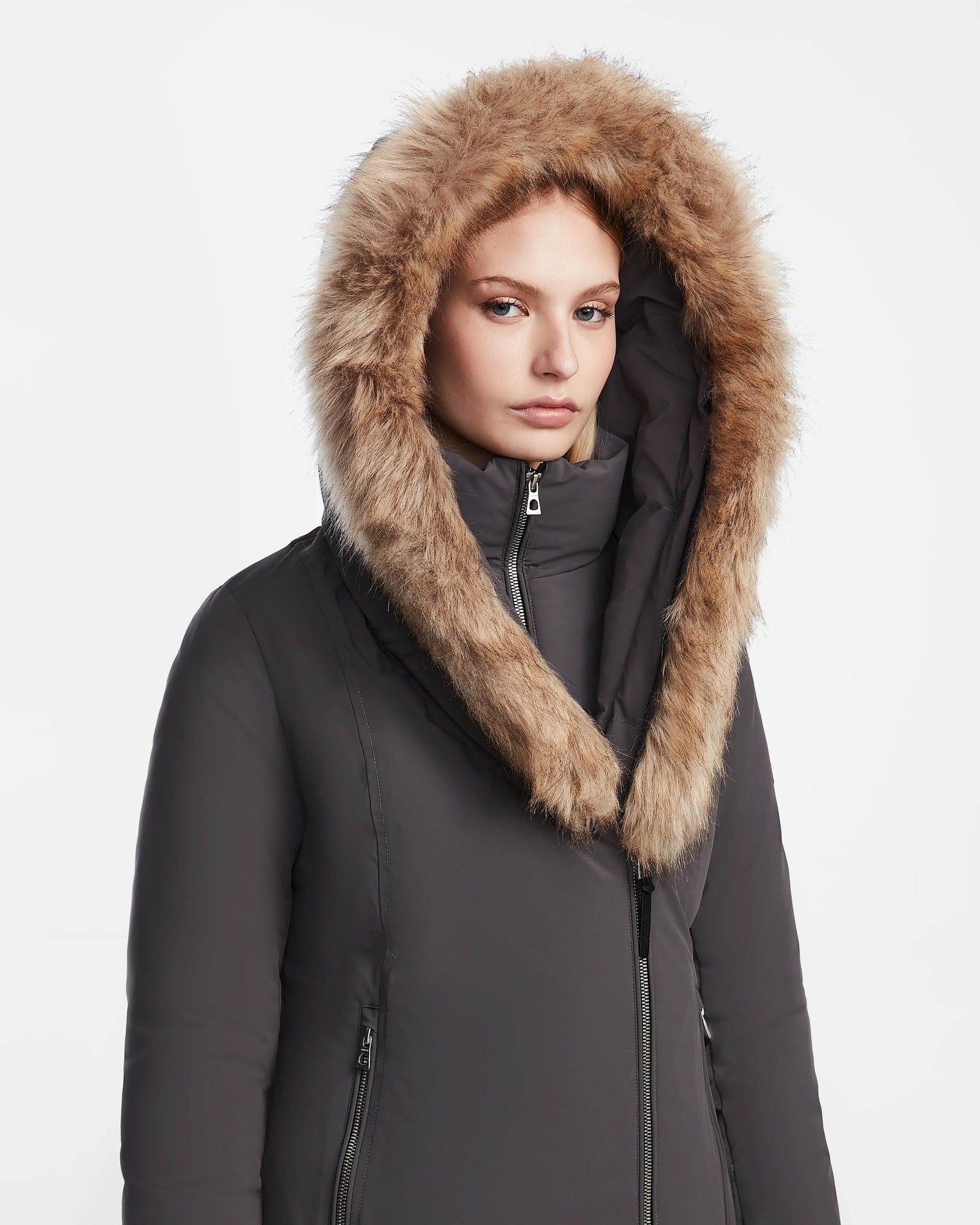 A woman wears the Rudsak AURORE - L123561 Grey fitted winter coat with a large, furry hood, standing against a plain white background and looking directly at the camera with a neutral expression.