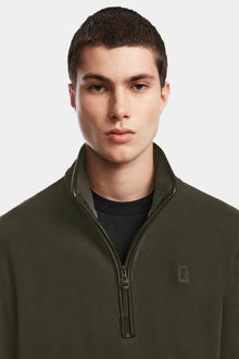 A young man with short dark hair wears the Rudsak BECK - 6524538 Army olive fleece pullover with vegan leather trims over a black shirt, standing against a plain light gray background.