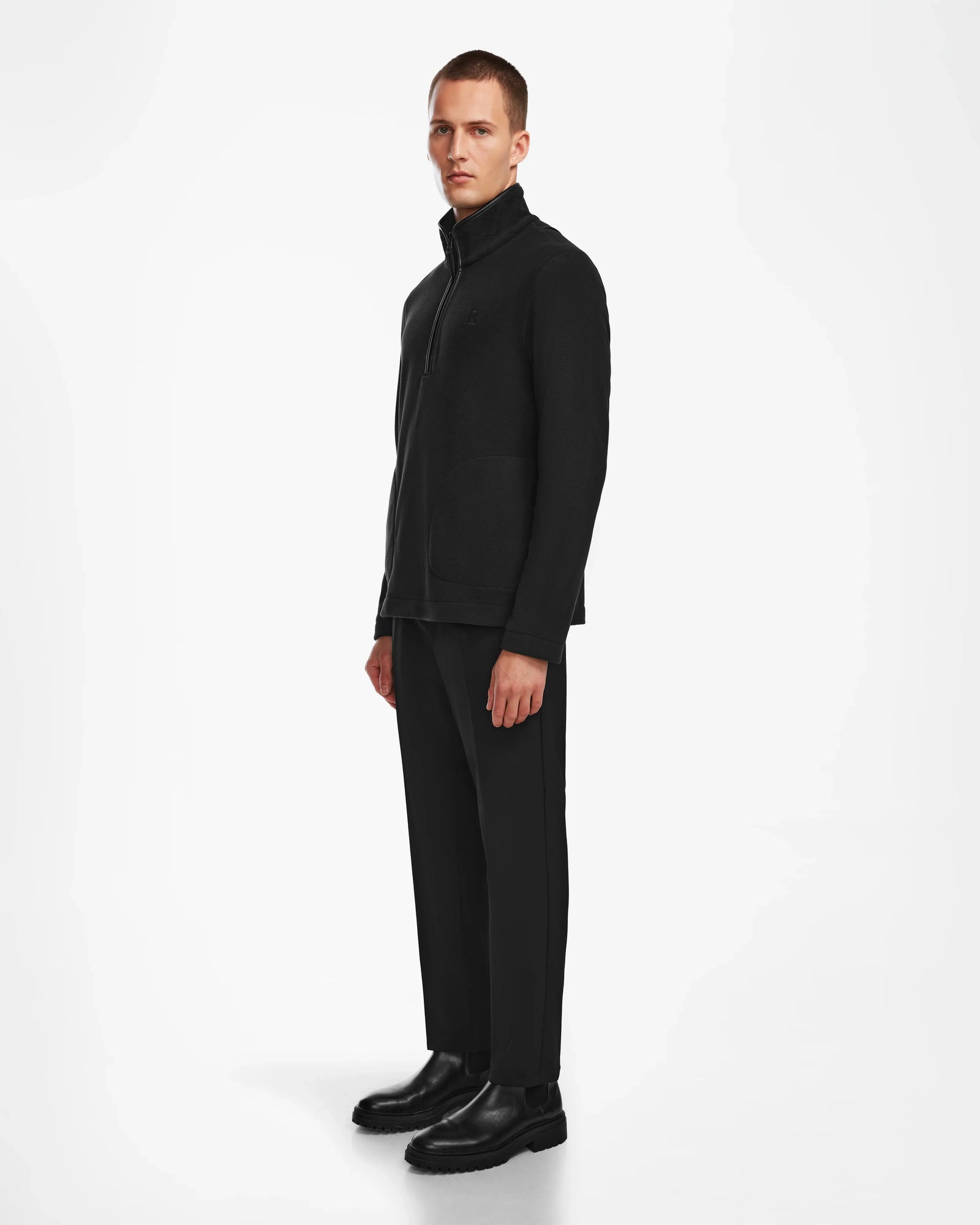 A man in a black suit wears the Rudsak BECK - 6524538 Black men’s fleece half-zip pullover, featuring stylish vegan leather trims for modern casual style.
