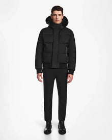 A man stands facing forward in a Rudsak DALLAS - M122501 black down bomber puffer coat with a fur-lined hood, paired with black pants and boots, set against a plain white background.