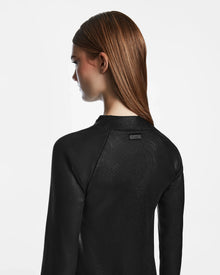 A woman with long, straight brown hair is seen from behind, wearing the Rudsak FAIZA - 8524579 mock-neck dress in textured black against a plain white background.