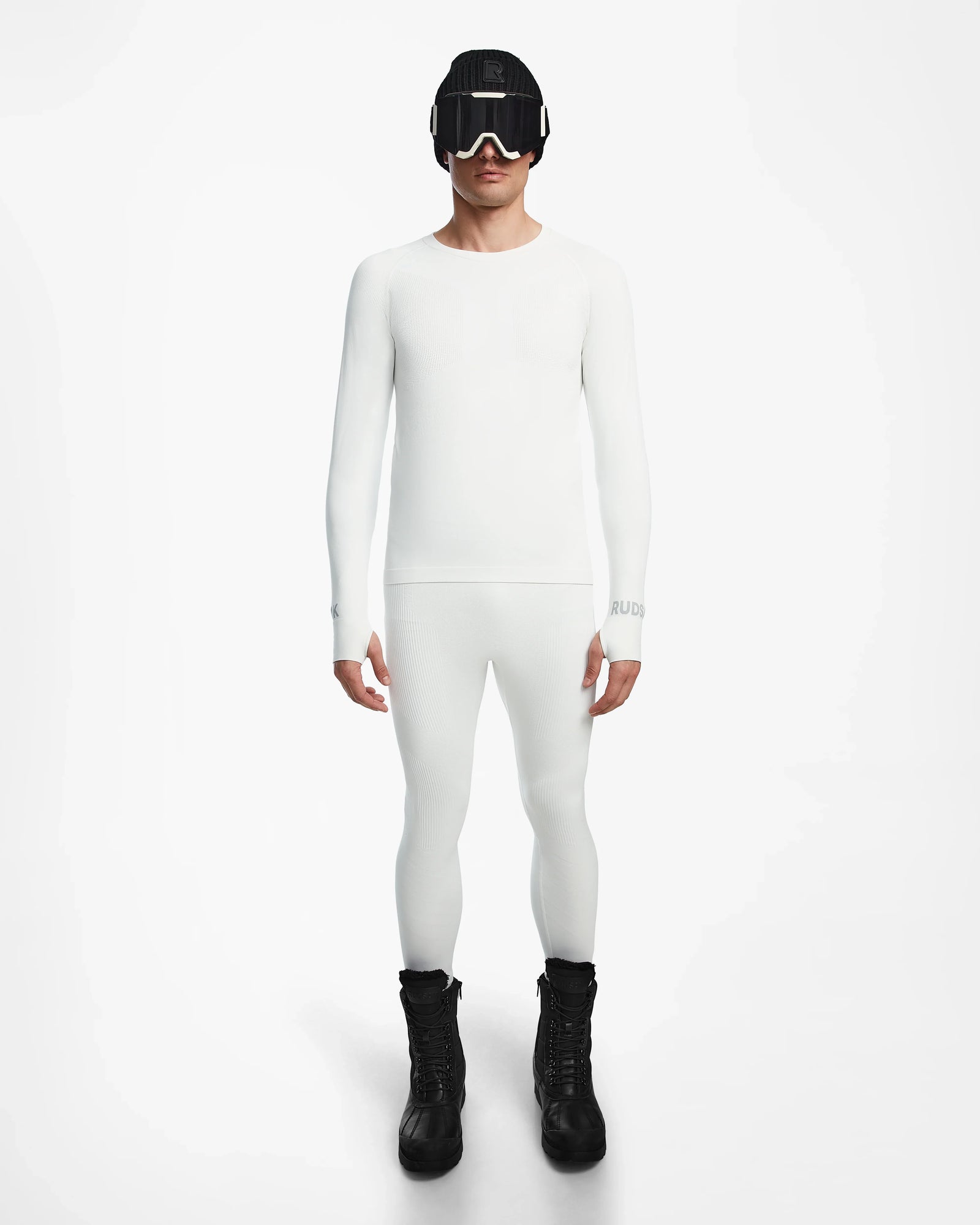 A person stands facing forward, wearing the Rudsak FRANC - 6524541 Iceland fitted white stretch base layer top and matching leggings, paired with black winter boots, ski goggles, and a beanie against a plain white background.